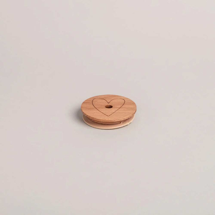 Der Eulenschnitt - Deckel Herz für Hohes Trinkglas ist ein runder Holzdeckel mit eingraviertem Herzdesign und einem zentralen Loch, dargestellt auf einem schlichten hellen Hintergrund.