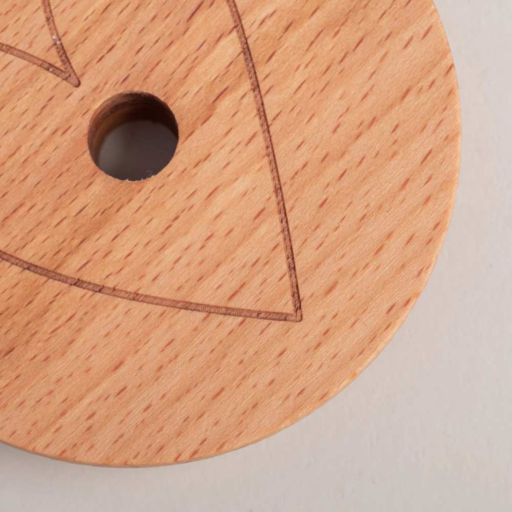 Eine Nahaufnahme des Eulenschnitt - Deckel Herz für Hohes Trinkglas, eines runden Holzdeckels mit einem zentralen Loch und teilweiser geometrischer Liniengravur auf der Oberfläche.