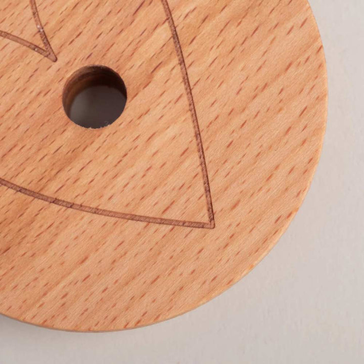 Eine Nahaufnahme des Eulenschnitt - Deckel Herz für Hohes Trinkglas, eines runden Holzdeckels mit einem zentralen Loch und teilweiser geometrischer Liniengravur auf der Oberfläche.