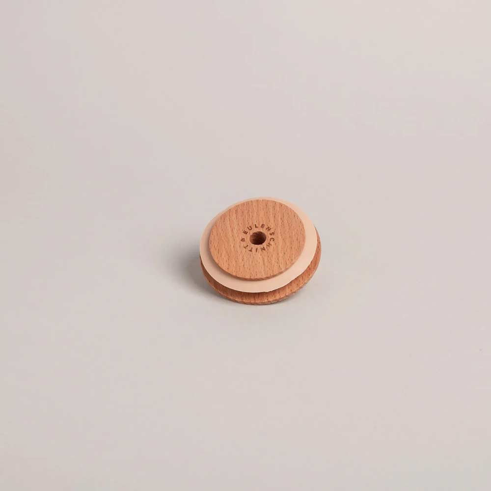 Der Eulenschnitt - Deckel Herz für Hohes Trinkglas, ein kleiner runder Holzdeckel mit einem herzförmigen Loch in der Mitte, ruht auf einer schlichten, hellen Unterlage.