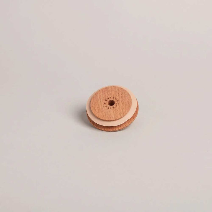 Der Eulenschnitt - Deckel Herz für Hohes Trinkglas, ein kleiner runder Holzdeckel mit einem herzförmigen Loch in der Mitte, ruht auf einer schlichten, hellen Unterlage.