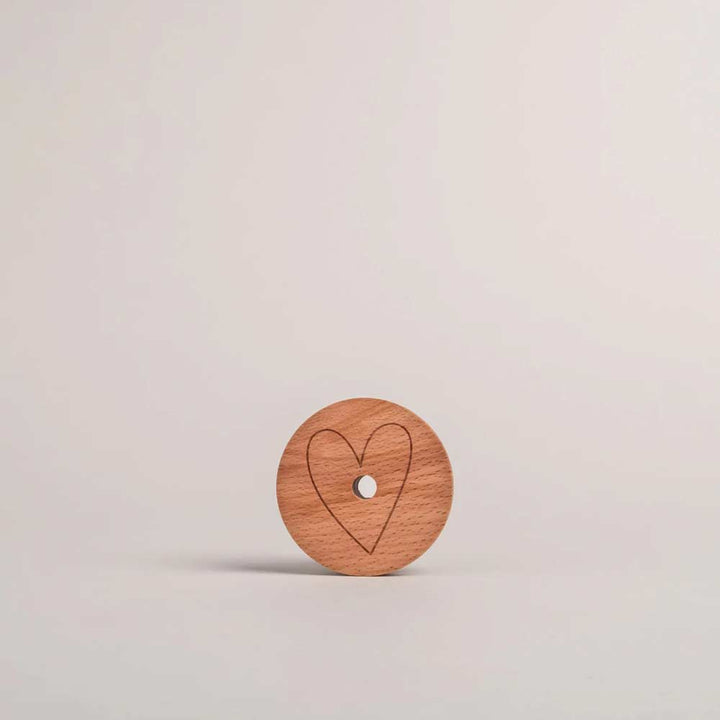 Der Eulenschnitt - Deckel Herz für Hohes Trinkglas, ein runder Holzdeckel mit Herz-Umrissgravur, steht aufrecht vor einem schlichten, hellen Hintergrund.