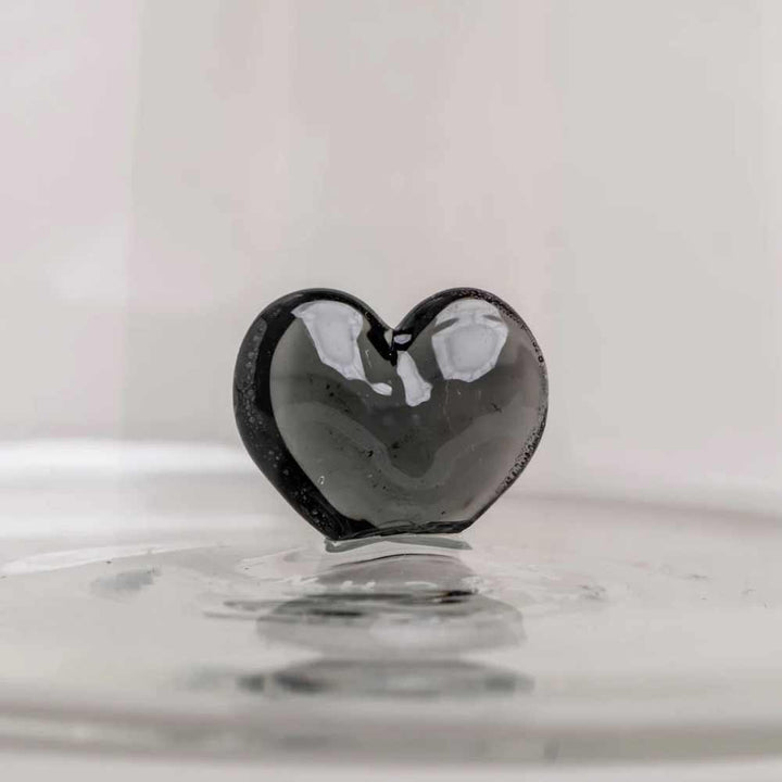 Die Eulenschnitt - Karaffe Herzfigur schwarz, eine glänzend schwarze Karaffe in Herzform, ruht elegant auf einer reflektierenden Oberfläche vor einem schlichten, hellen Hintergrund.