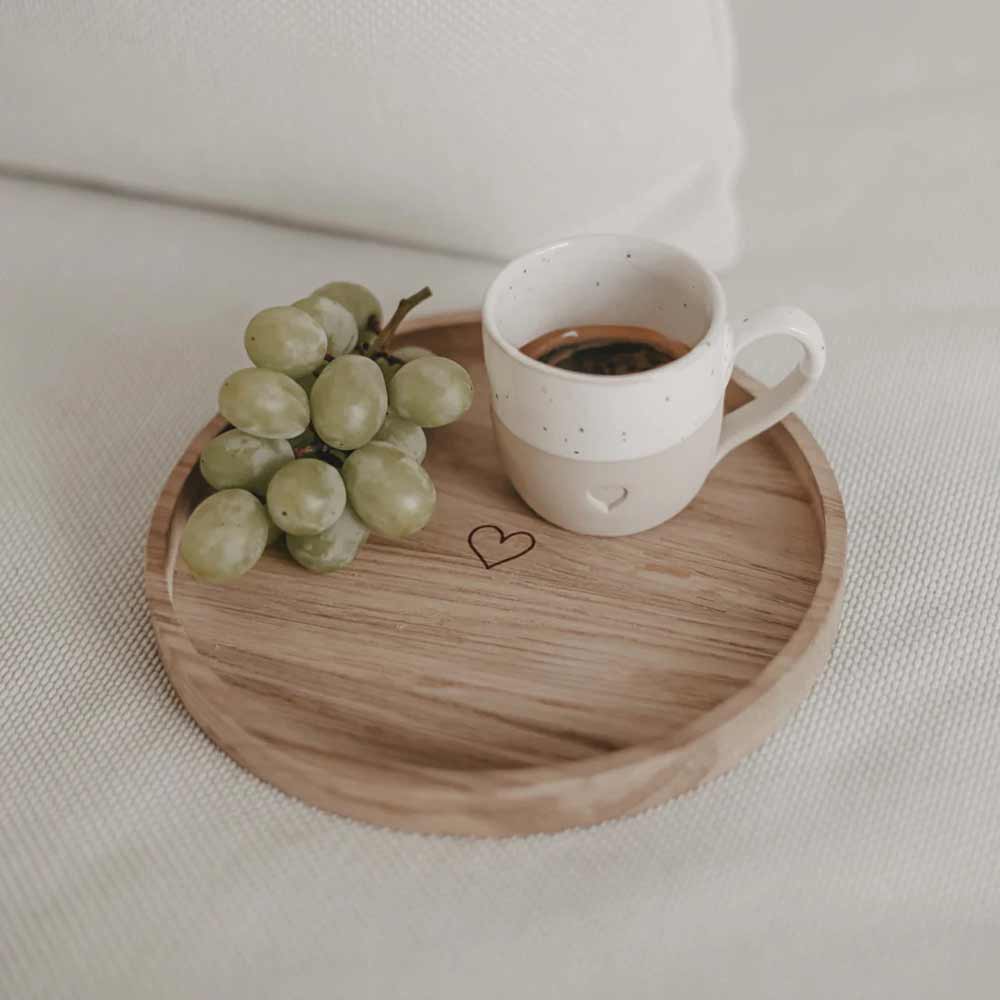 Eine kleine Traube grüner Weintrauben und eine Tasse schwarzen Kaffee stehen auf dem Eulenschnitt - Mini Tablett rund Herz, einem runden Holztablett mit Herzdesign auf einer leicht strukturierten Oberfläche.