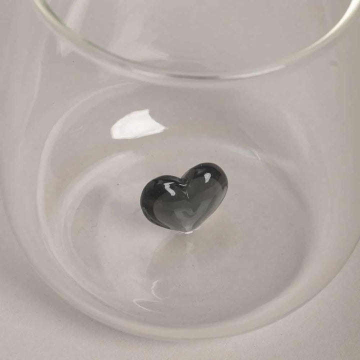 Eine Eulenschnitt - Trinkglas Herzfigur schwarz mit einem kleinen schwarzen Glasherz steht leer auf einer hellen Oberfläche.