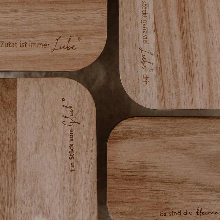 Vier Eulenschnitt-Vorratsbehälter aus Glas mit Holzdeckel, jeweils mit eingravierten deutschen Sprüchen über Liebe und Glück, dicht an dicht auf einer braunen Fläche angeordnet.