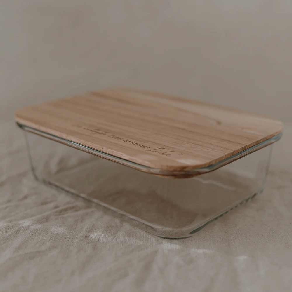 Der Eulenschnitt Vorratsbehälter Glas mit Holzdeckel und Spruch steht auf einer strukturierten, neutralfarbenen Stoffoberfläche.