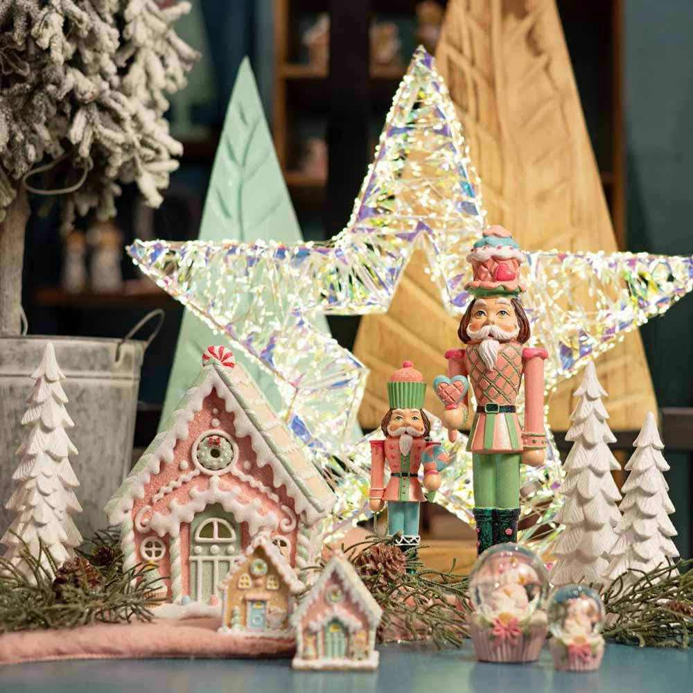 Eine festliche Präsentation mit dem Weihnachtsbaumschmuck Lebkuchenhaus von G. Wurm, begleitet von einem leuchtenden Stern, Nussknackerfiguren, schneebedeckten Bäumen und einer Schneekugel.