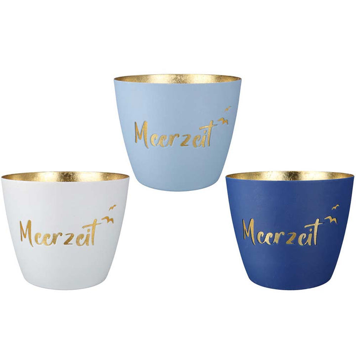 Der Gilde Windlicht Meerzeit Schriftzug besteht aus drei Tassen in Weiß, Hellblau und Dunkelblau mit goldener Innenseite und „Meerzeit“ mit fliegenden Vögeln in Gold auf der Vorderseite.