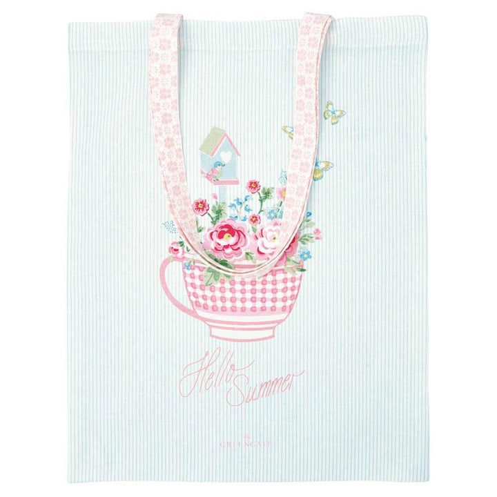 Die GreenGate - Alma Summer Stofftasche weiß ist eine weiße Tragetasche mit hellblauen Streifen, rosafarbenen Henkeln, einer mit Blumen und Schmetterlingen gefüllten Teetasse und dem Aufdruck "Hello Summer" unterhalb des Designs.
