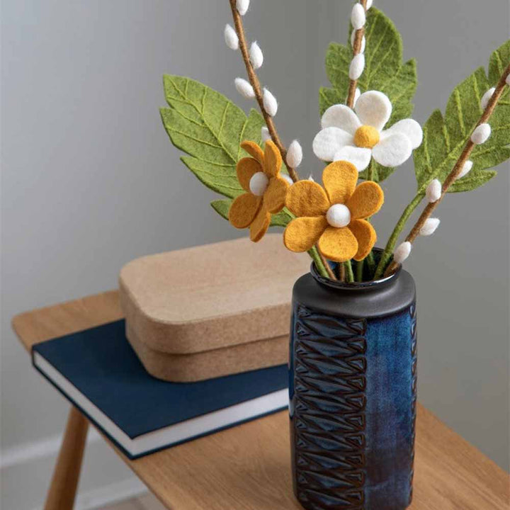 Ein Gry & Sif - Weidenkätzchen Filz mit Filzblumen auf einem Holztisch neben einem Buch und einer Schachtel.