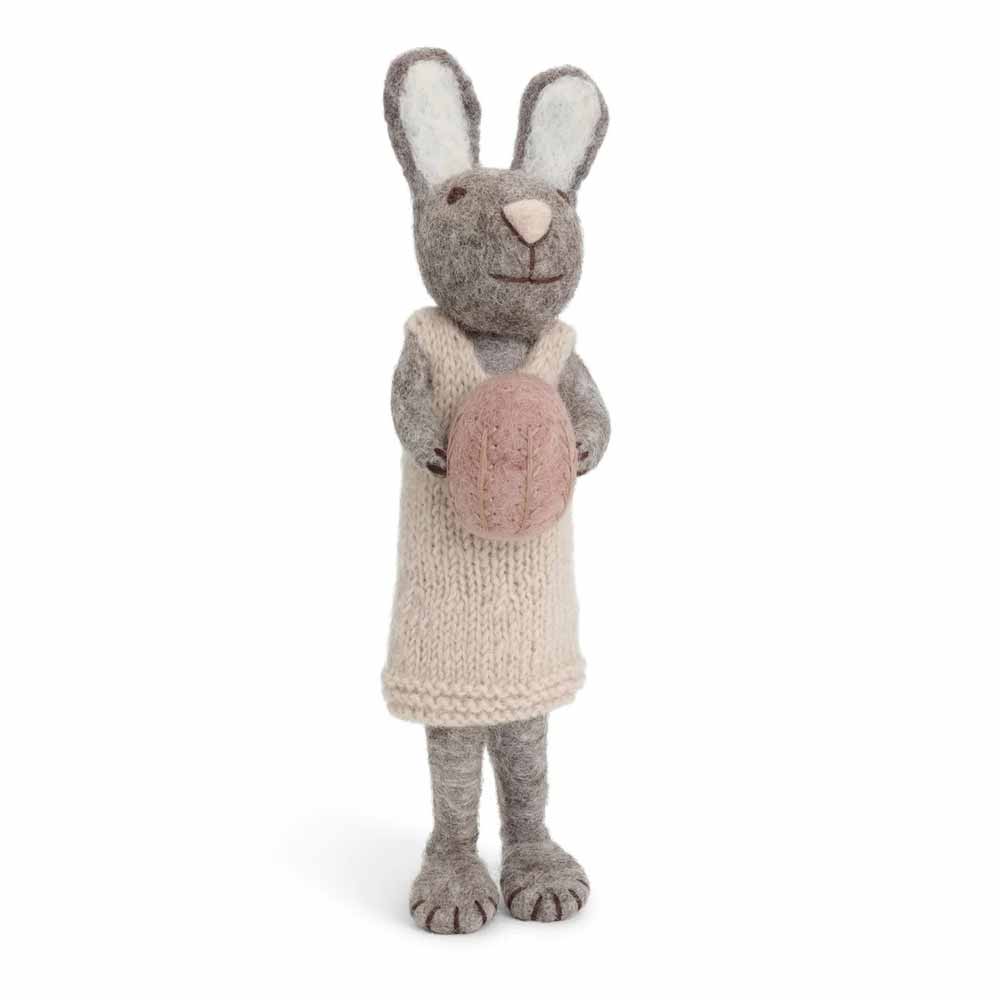 Ein hellgrauer Gry & Sif - Hase Filz mit Ei in einem Strickkleid mit einem Ei in der Hand.