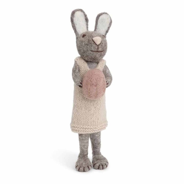 Ein hellgrauer Gry & Sif - Hase Filz mit Ei in einem Strickkleid mit einem Ei in der Hand.