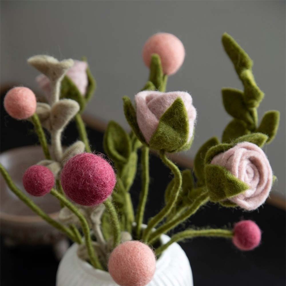 Eine Nahaufnahme einer Vase mit Gry & Sif – Rose Filz-Blumen in Rosa- und Grüntönen, mit detaillierten Texturen auf dunklem Hintergrund.