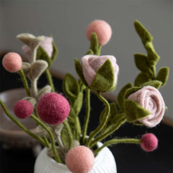 Eine Nahaufnahme einer Vase mit Gry & Sif – Rose Filz-Blumen in Rosa- und Grüntönen, mit detaillierten Texturen auf dunklem Hintergrund.