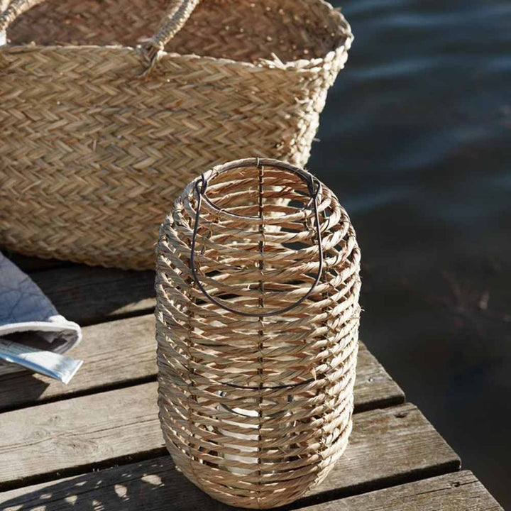 Geflochtene Körbe auf einer Ib Laursen - Laterne Seegras und Metall mit Glaseinsatz neben Wasser.