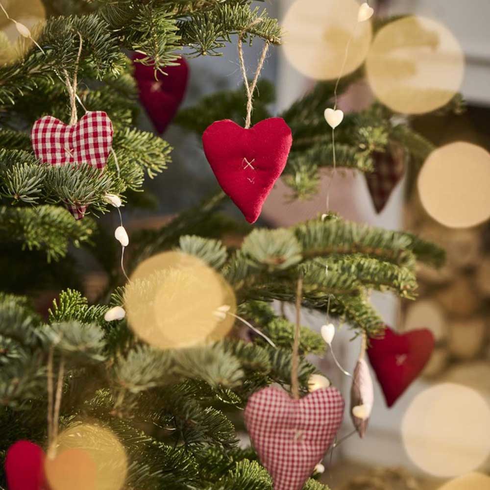 Die Stoffornamente „My Nostalgic Christmas Heart“ von Ib Laursen schmücken den Weihnachtsbaum, ergänzt durch schimmernde Lichterketten.
