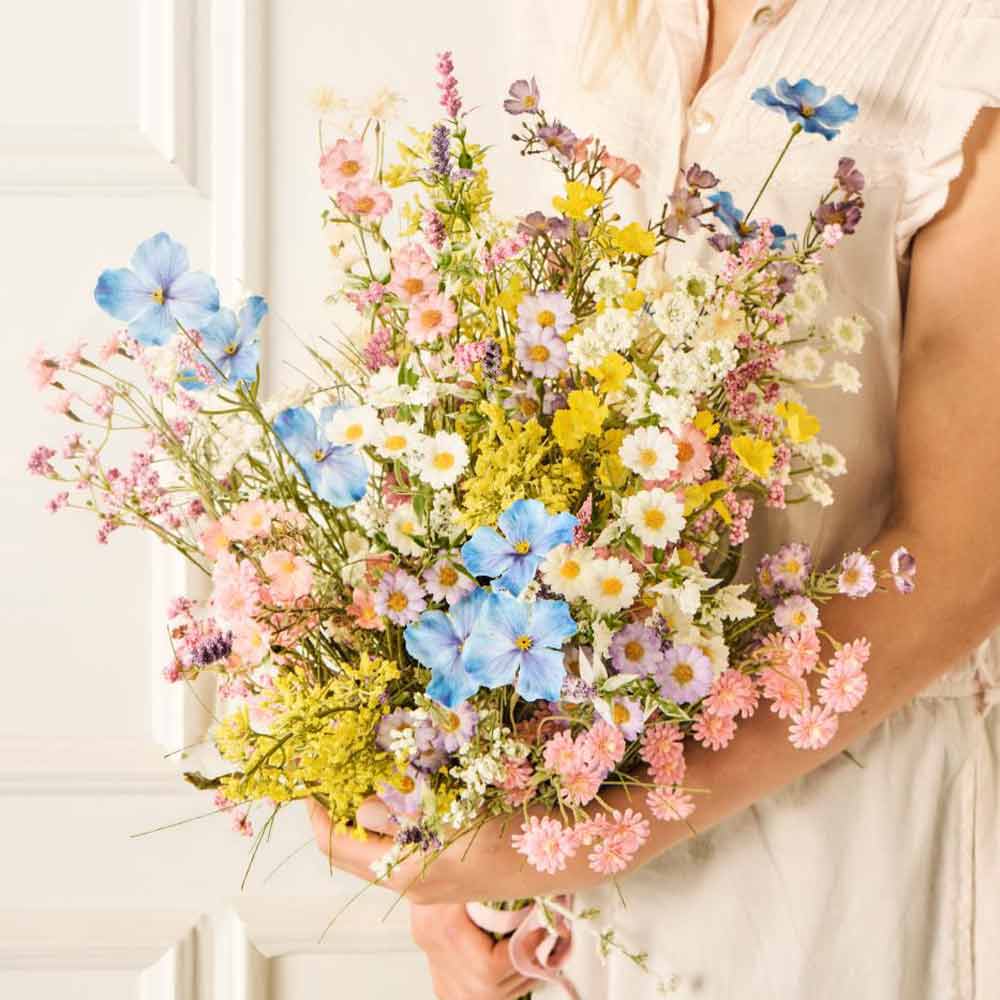 Person hält die Ib Laursen – Blume rosa/grün, einen großen Strauß mit verschiedenen pastellfarbenen Wildblumen in Blau-, Gelb-, Rosa- und Weißtönen.
