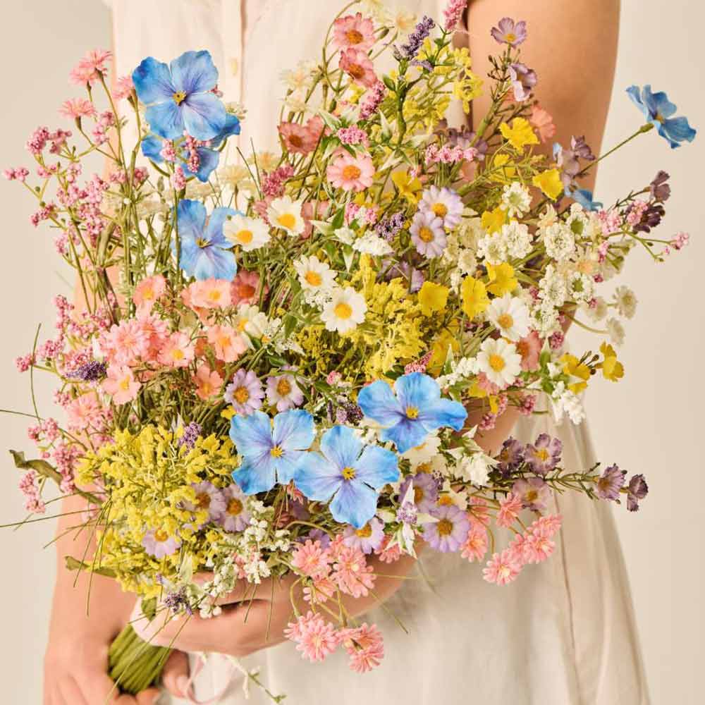 Eine Person in einem ärmellosen, leichten Kleid hält die Ib Laursen – Blume rosa/grün, einen großen Strauß verschiedener Wildblumen in Rosa- und Grüntönen.