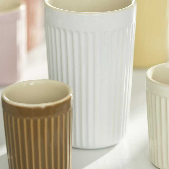 Drei Ib Laursen - Cafe Latte Becher mit Rillen Mynte in verschiedenen Größen und neutralen Farben sind dicht auf einer sonnenbeschienenen Oberfläche angeordnet.