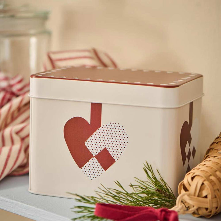 Gebäckdose von Ib Laursen mit einem eingewebten Weihnachtsherzdesign auf einem Regal, kombiniert mit einem gestreiften Tuch und Grünpflanzen.