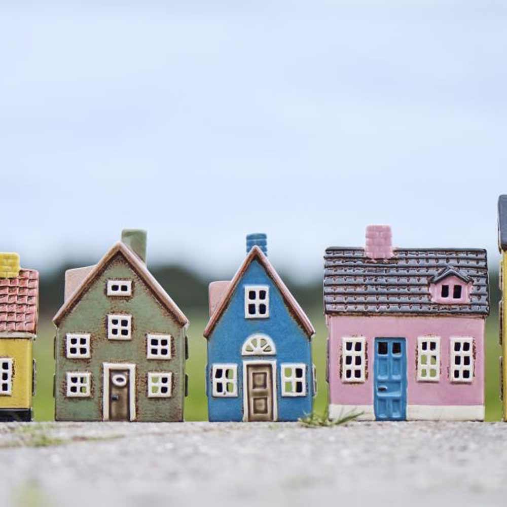 Fünf Ib Laursen „Haus für Teelicht My Home Town blaue Tür“-Kerzenhalter stehen im Freien auf einer ebenen Fläche, im Hintergrund sind ein unscharfer Himmel und ein Feld zu sehen.