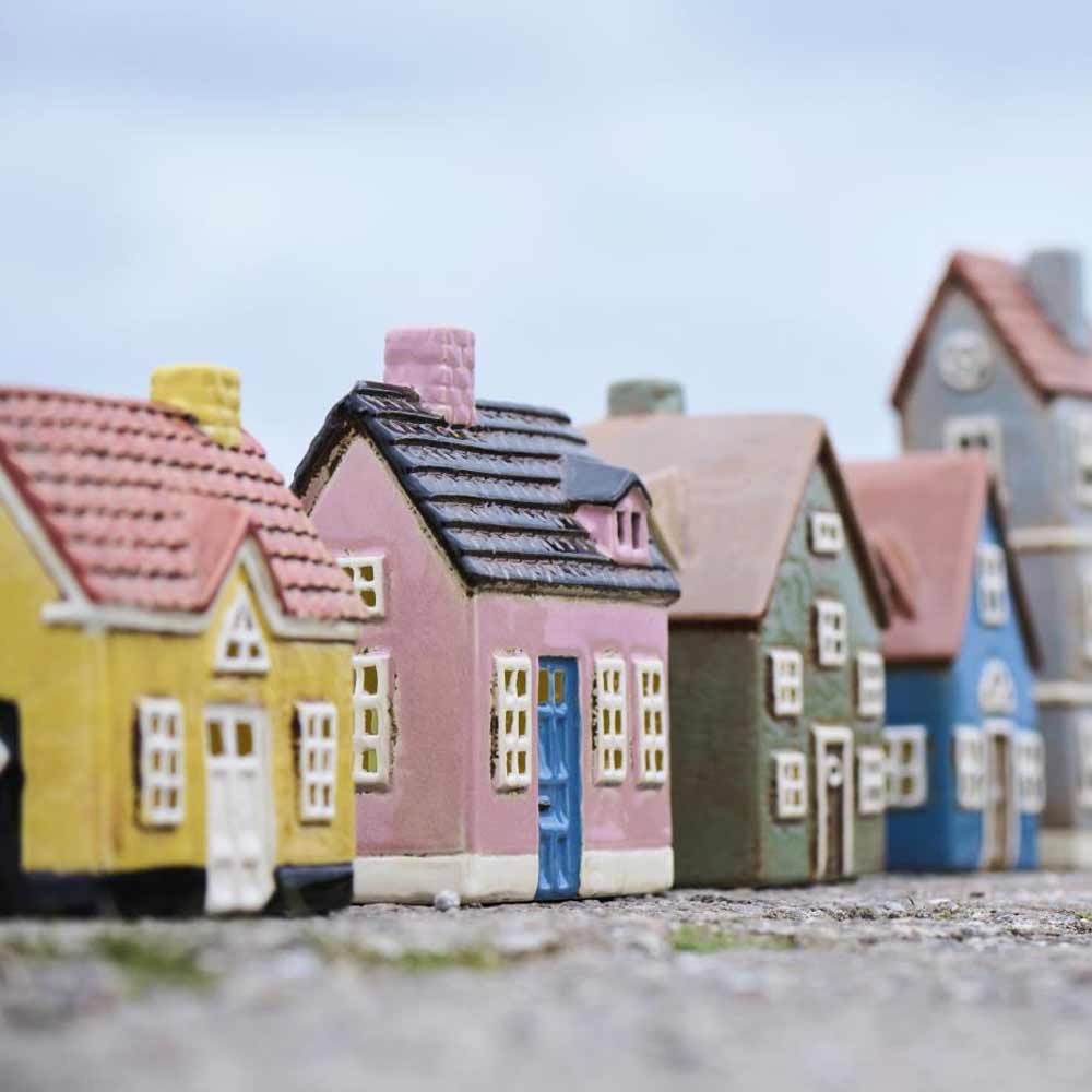 Ib Laursen – Haus für Teelicht „My Home Town“ blaue Tür: Kleines, farbenfrohes Modellhaus mit detailliertem Dach und Fenstern, im Freien auf einer strukturierten Oberfläche mit unscharfem Himmel im Hintergrund platziert.