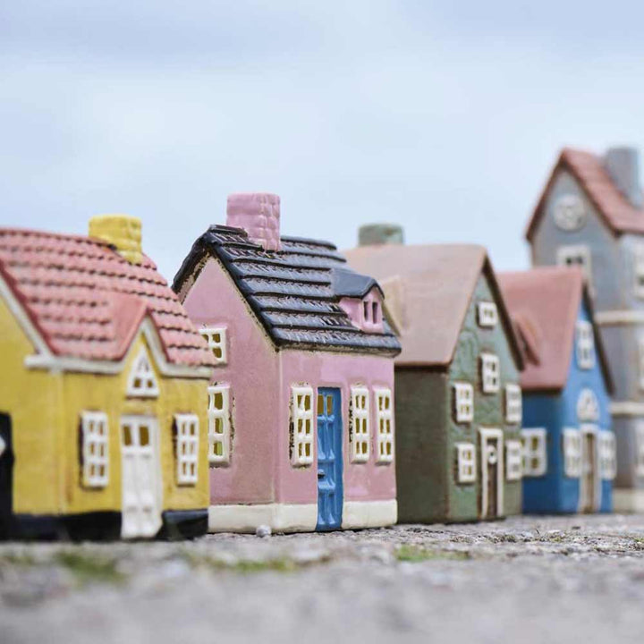 Ib Laursen – Haus für Teelicht „My Home Town“ blaue Tür: Kleines, farbenfrohes Modellhaus mit detailliertem Dach und Fenstern, im Freien auf einer strukturierten Oberfläche mit unscharfem Himmel im Hintergrund platziert.