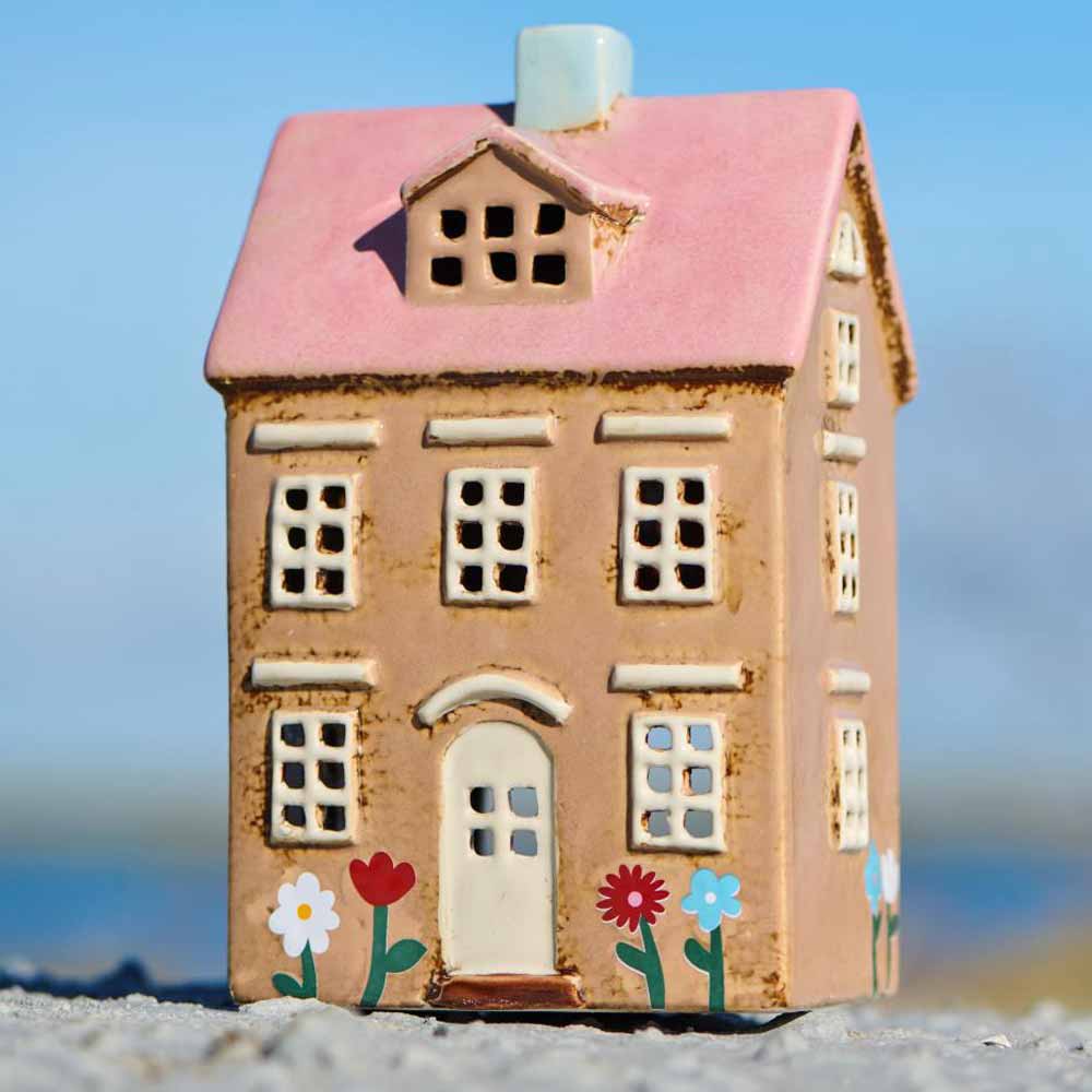 Das Ib Laursen Haus für Teelicht Nyhavn hat ein rosafarbenes Dach, cremefarbene Wände und gemalte Blumen an der Tür - ein charmantes Keramikhaus, das sich perfekt für Teelichter eignet.