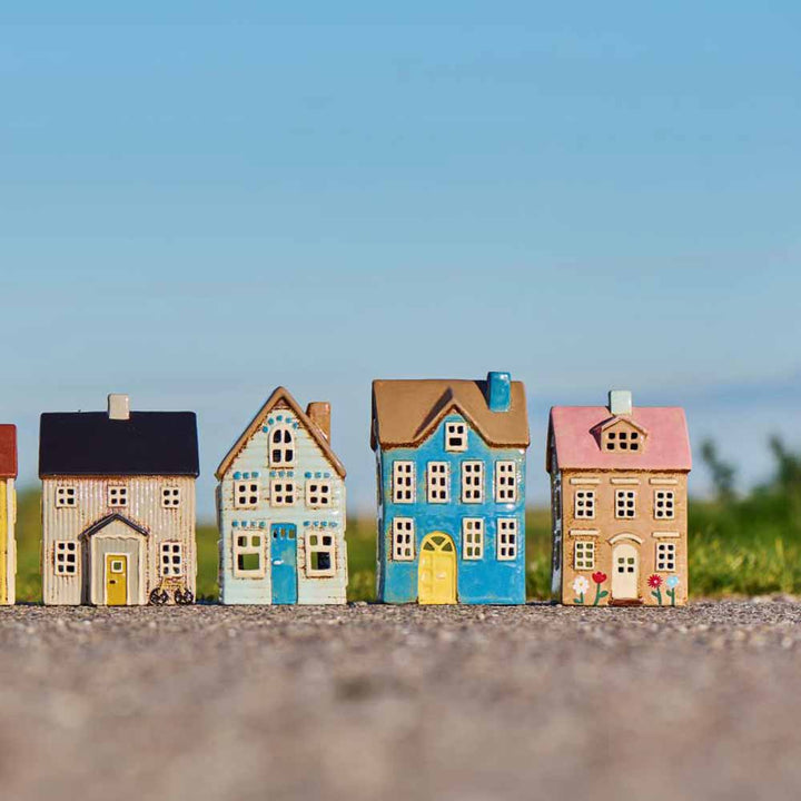 Vier Ib Laursen-Modelle "Haus für Teelicht Nyhavn Blumen und rosa Dach" sind im Freien auf einer ebenen Fläche aufgereiht, mit Gras und blauem Himmel im Hintergrund.