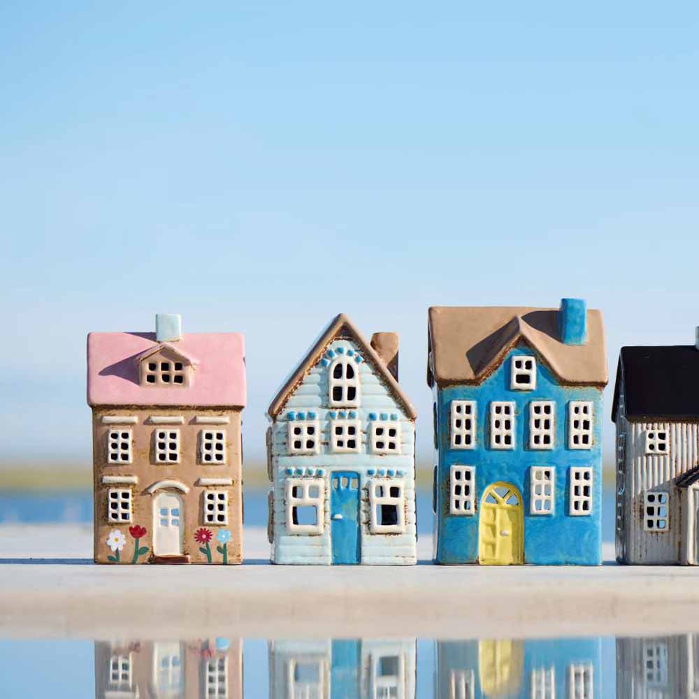 Das Ib Laursen Haus für Teelicht Nyhavn Blumen und rosa Dach steht unter freiem Himmel mit seiner pastellfarbenen Keramikfassade, in der sich der blaue Himmel spiegelt.