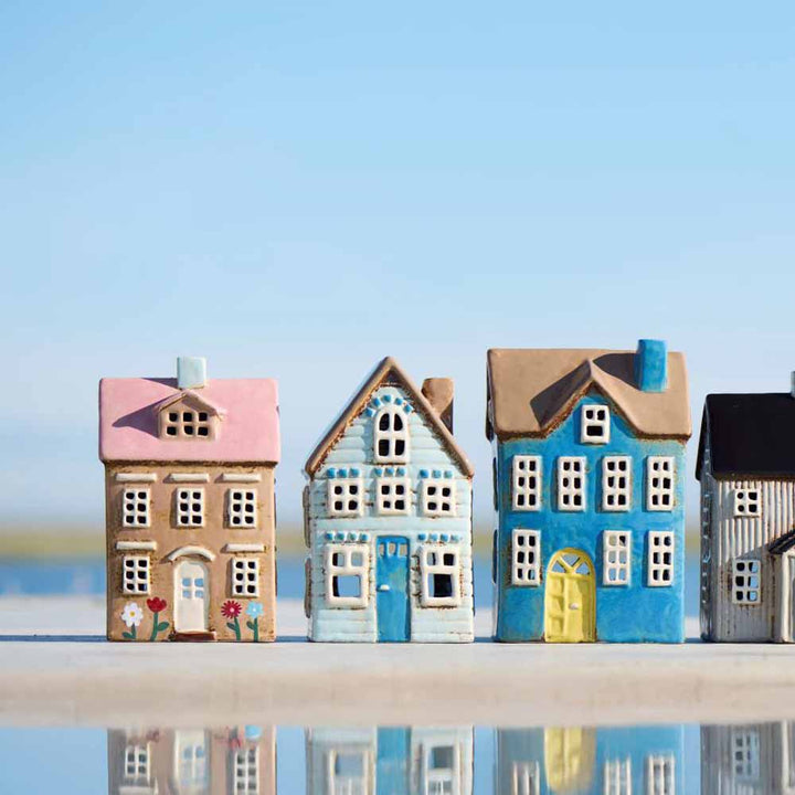 Das Ib Laursen Haus für Teelicht Nyhavn Blumen und rosa Dach steht unter freiem Himmel mit seiner pastellfarbenen Keramikfassade, in der sich der blaue Himmel spiegelt.