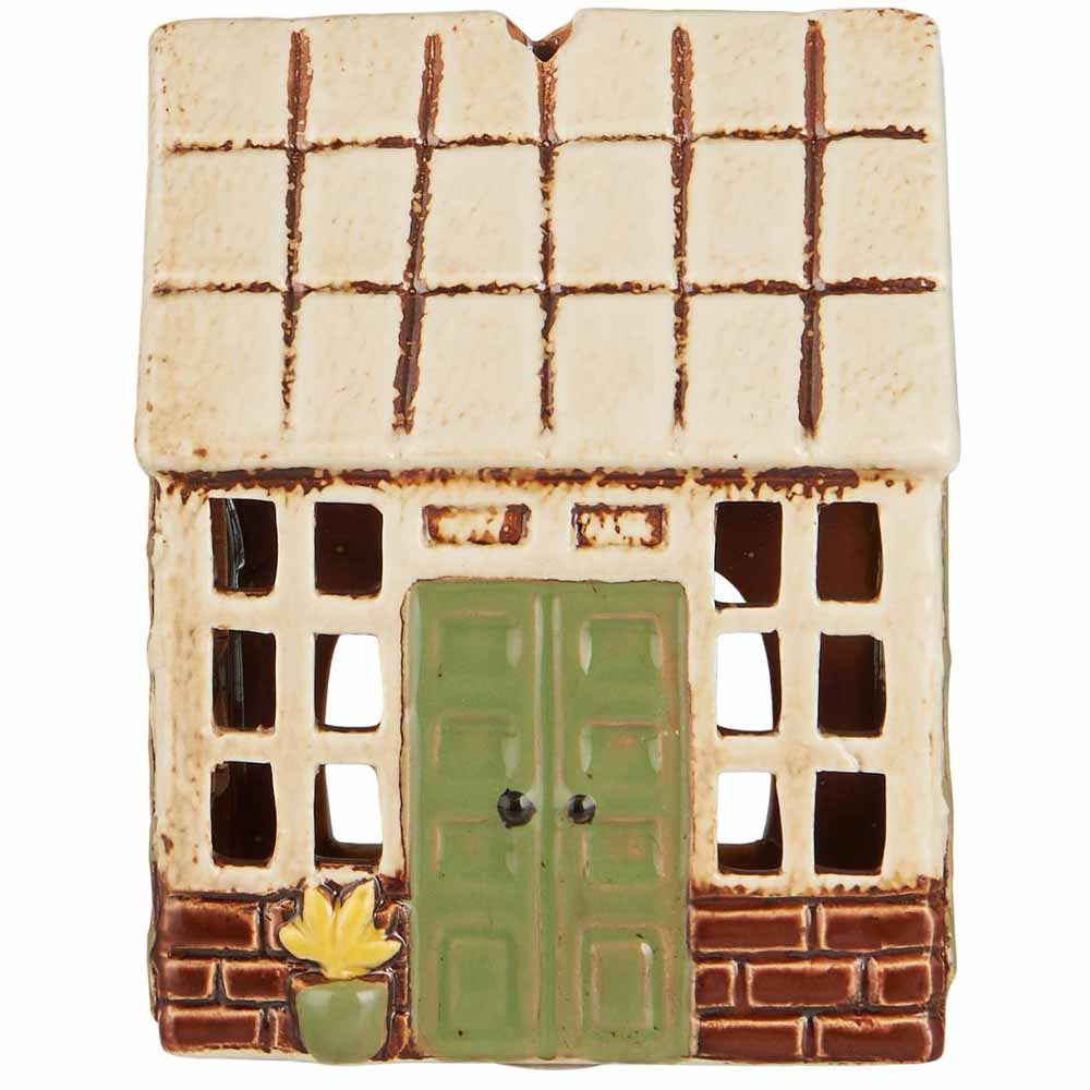Das Ib Laursen - Haus für Teelicht Orangerie ist ein Ornament in Form eines Keramikhauses mit einer grünen Doppeltür, Gitterfenstern, einer gelben Topfpflanze und einem cremefarbenen und braunen Dach.