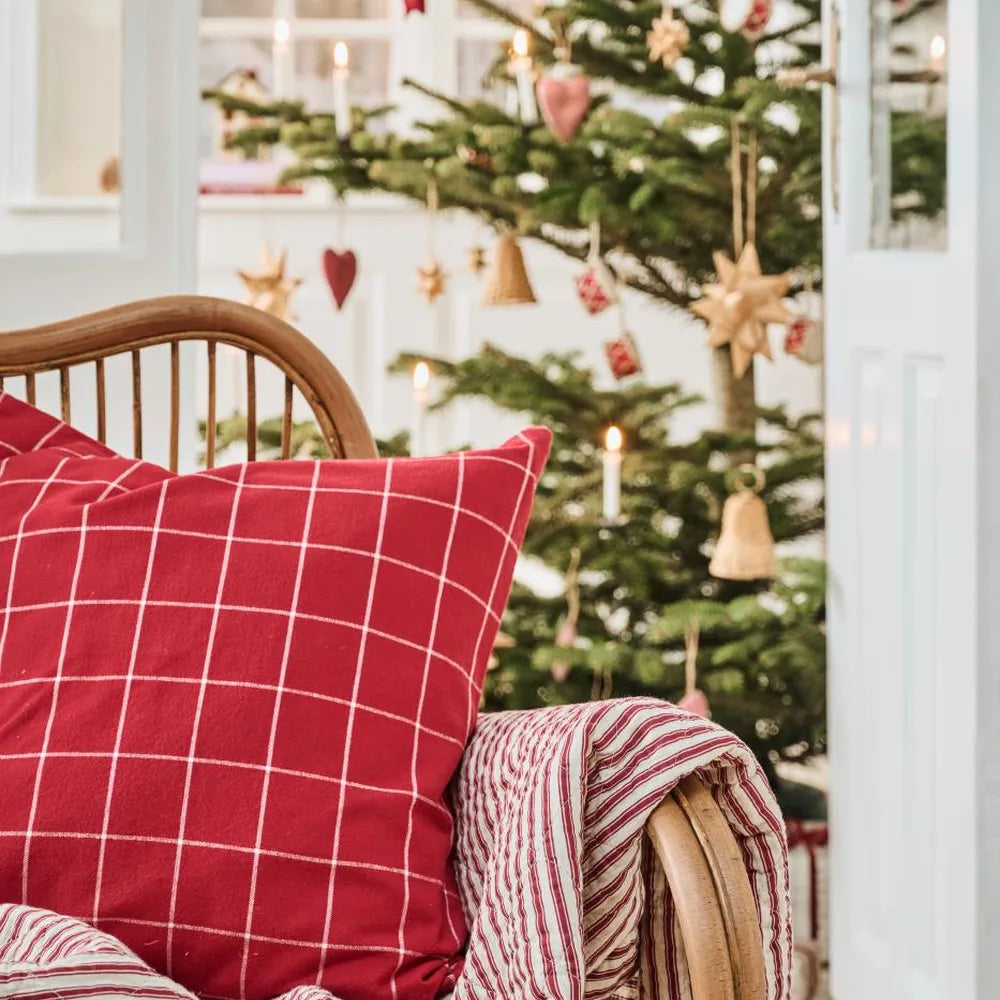 Rotes Silja-Karokissen auf einem Holzstuhl mit gestreiftem Stoff, im Hintergrund ein geschmückter Weihnachtsbaum