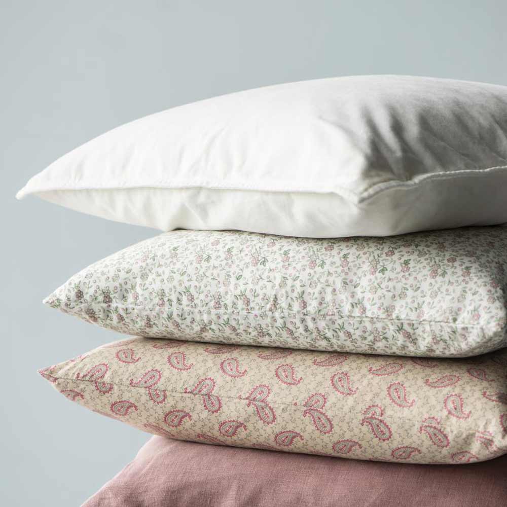 Ein Stapel aus drei Kissen: oben der Ib Laursen Kissenbezug Velours Butter Cream, in der Mitte ein Kissen mit Blumenmuster und unten ein Kissen mit rosa Paisleymuster.
