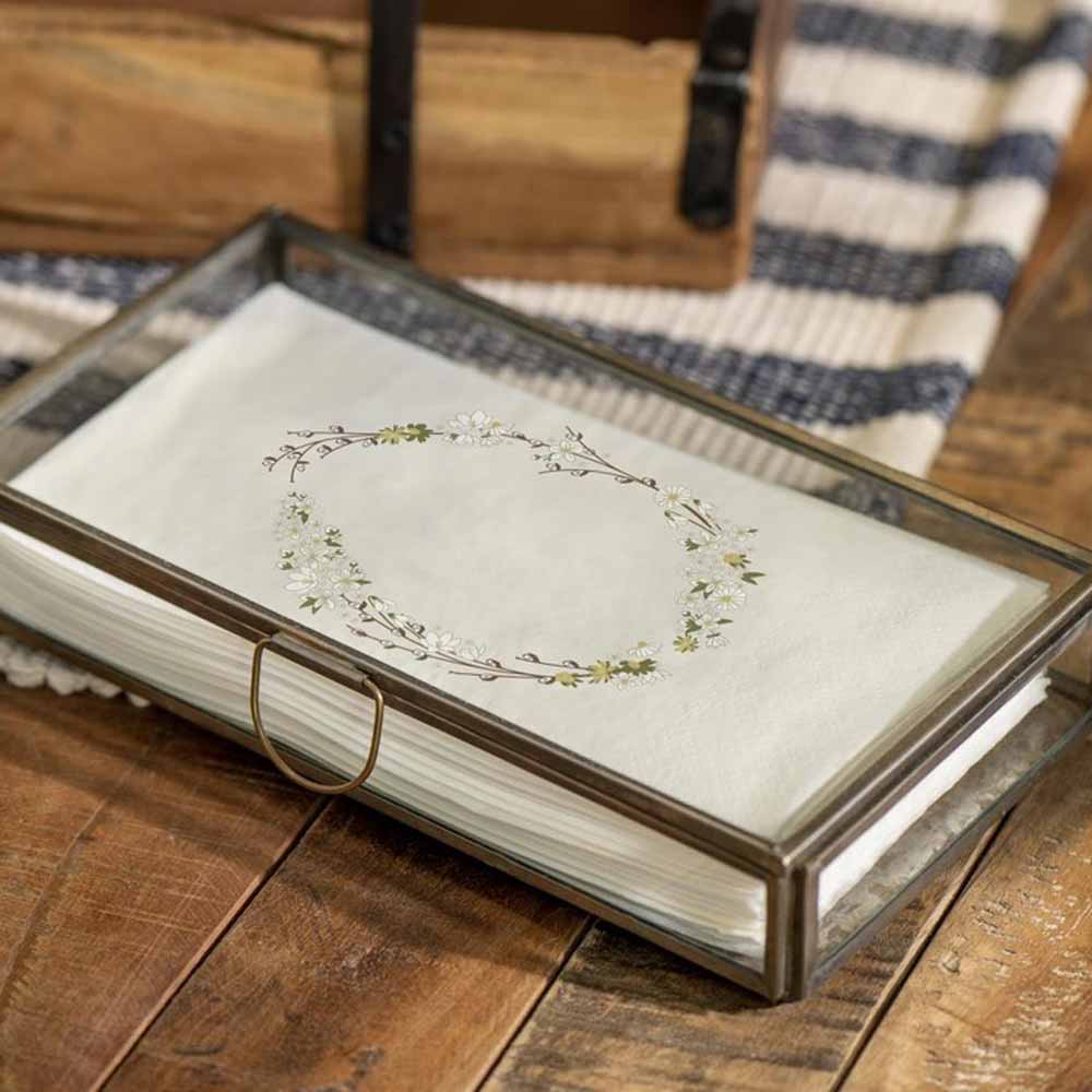 Ein dickes Buch mit einem Blumenmuster auf der offenen Seite, das auf einer Holzoberfläche ruht, mit einem schwarzen Metallelement und teilweise sichtbarer Ib Laursen - Serviette Osterei 16 Stück.