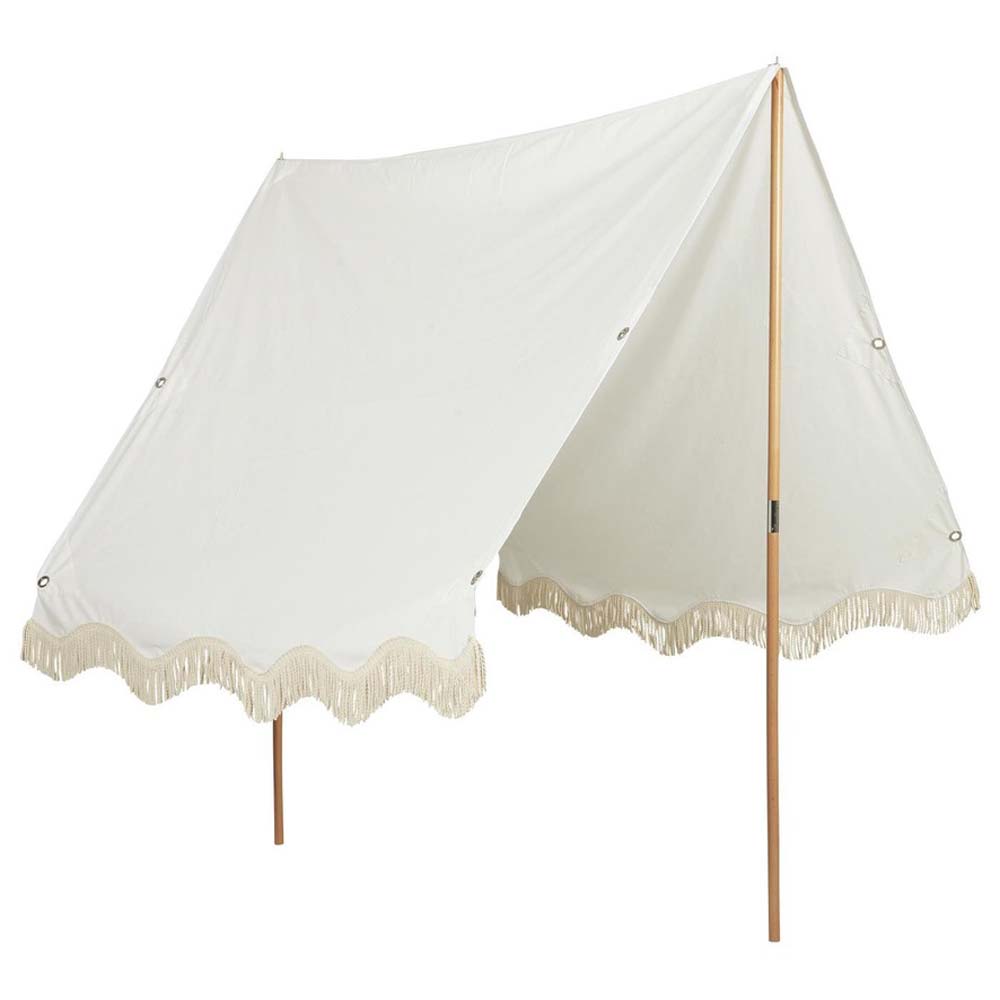 Ein weißes Segeltuchzelt mit Fransenbesatz an der Unterkante wird von Holzstangen getragen. Das Ib Laursen - Sonnensegel weiß mit naturfarbigen Fransen ist auf einer Seite offen und ermöglicht den Eingang.