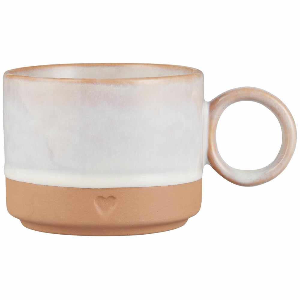 Der Becher von Ib Laursen hat einen runden Henkel, eine weiße obere Hälfte und einen unglasierten Terrakotta-Boden, der mit einem kleinen Herzaufdruck verziert ist.