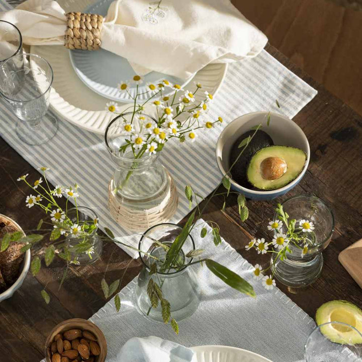 A Ib Laursen - Tischset staubig blau mit weissen Streifen mit Tellern und Gläsern und Blumen.