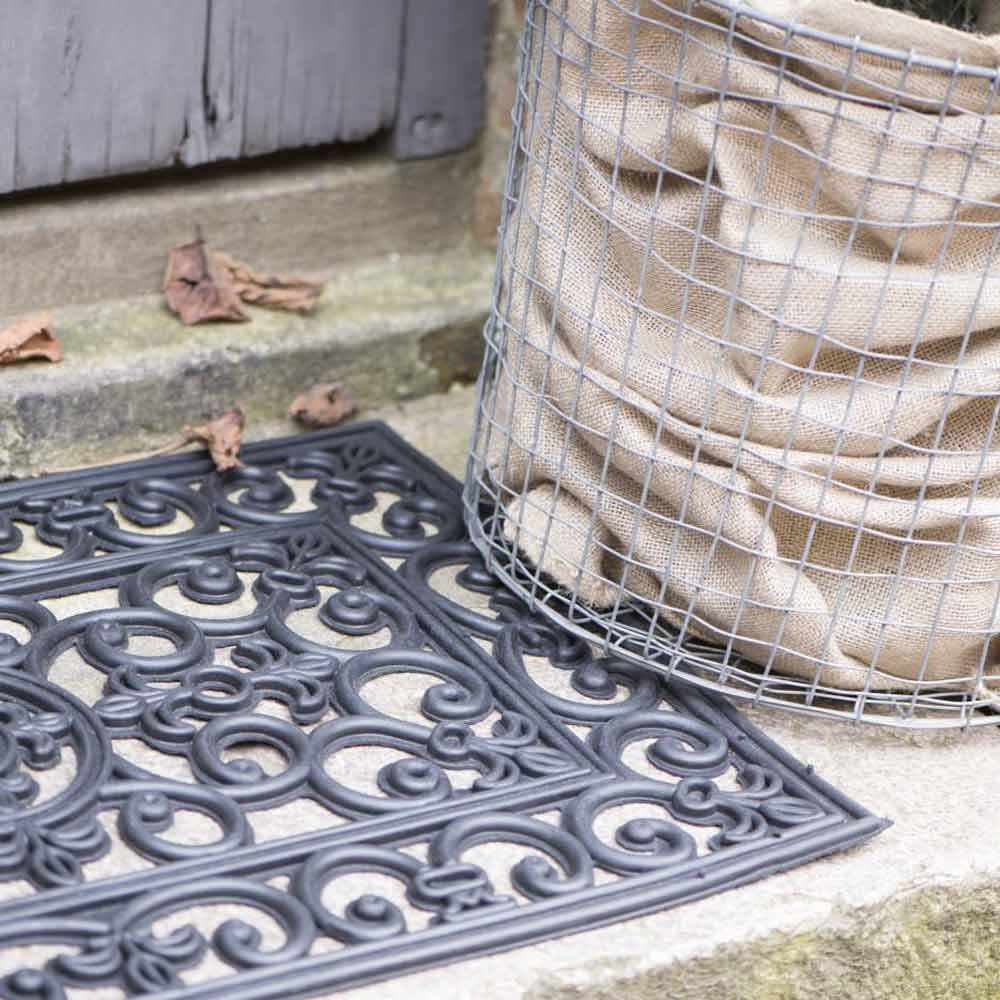 Ein Sack Kartoffeln, befestigt in einem Drahtgeflechtkäfig, neben einer Ib Laursen - Türmatte Gummi Filigran auf Betonstufen mit verstreuten Blättern.