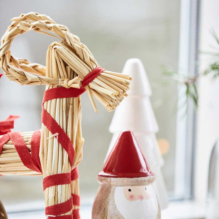 Ib Laursens Weihnachtsziege mit rotem Band My Nostalgic steht neben einer hölzernen Weihnachtsmannfigur und einem weißen Baumschmuck auf einer Fensterbank.