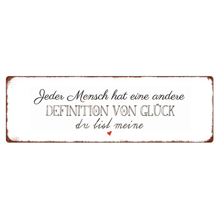 Auf einem rechteckigen Schild mit weißem Hintergrund und rostfarbenem Rand steht der deutsche Text: „Jeder Mensch hat eine andere Definition von Glück, du bist meine“ mit einem kleinen roten Herz am unteren Rand. Der Produktname lautet Interluxe Metallschild – Jeder Mensch hat eine andere Definition von Glück.