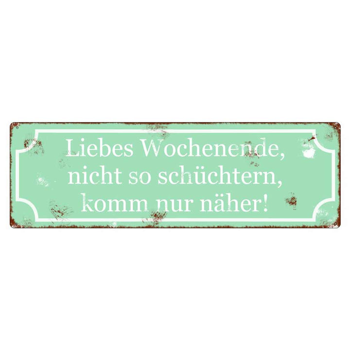 Auf einem rechteckigen grünen Schild mit abgenutzten Kanten steht in weißem deutschen Text: „Interluxe Metallschild – Liebes Wochenende nicht so schüchtern“.