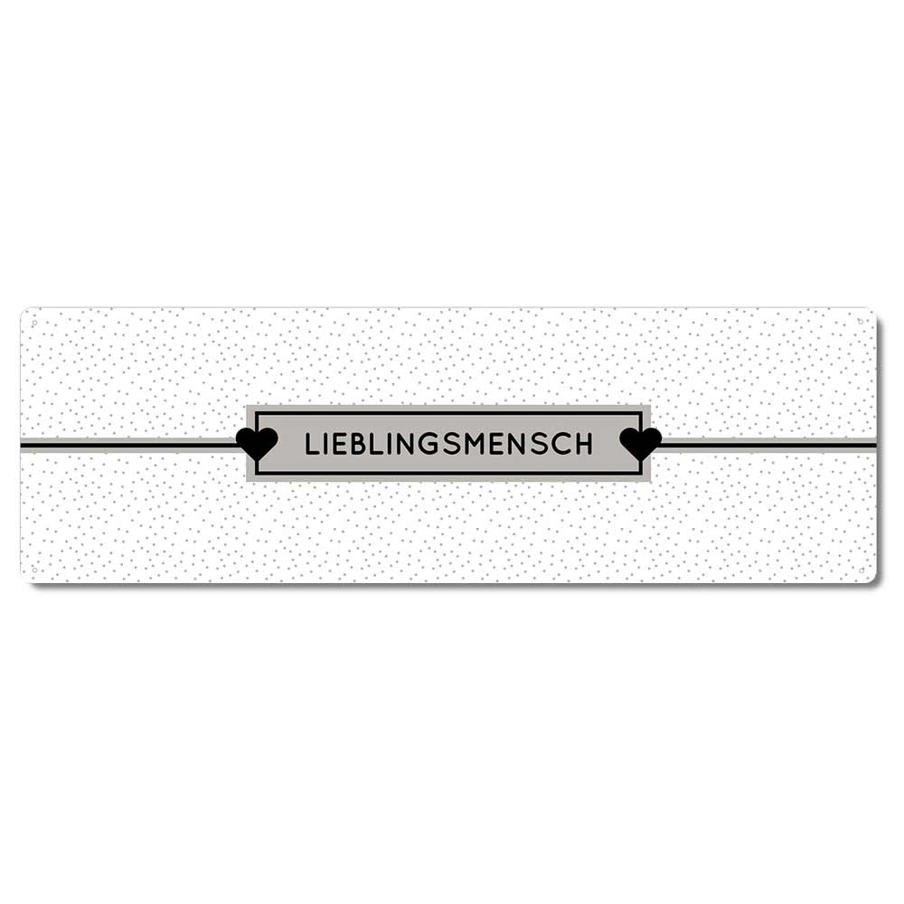 Ein rechteckiges weißes Schild mit kleinen schwarzen Punkten und der Aufschrift „Interluxe Metallschild – Lieblingsmensch“ in der Mitte, flankiert von zwei schwarzen Herzen.