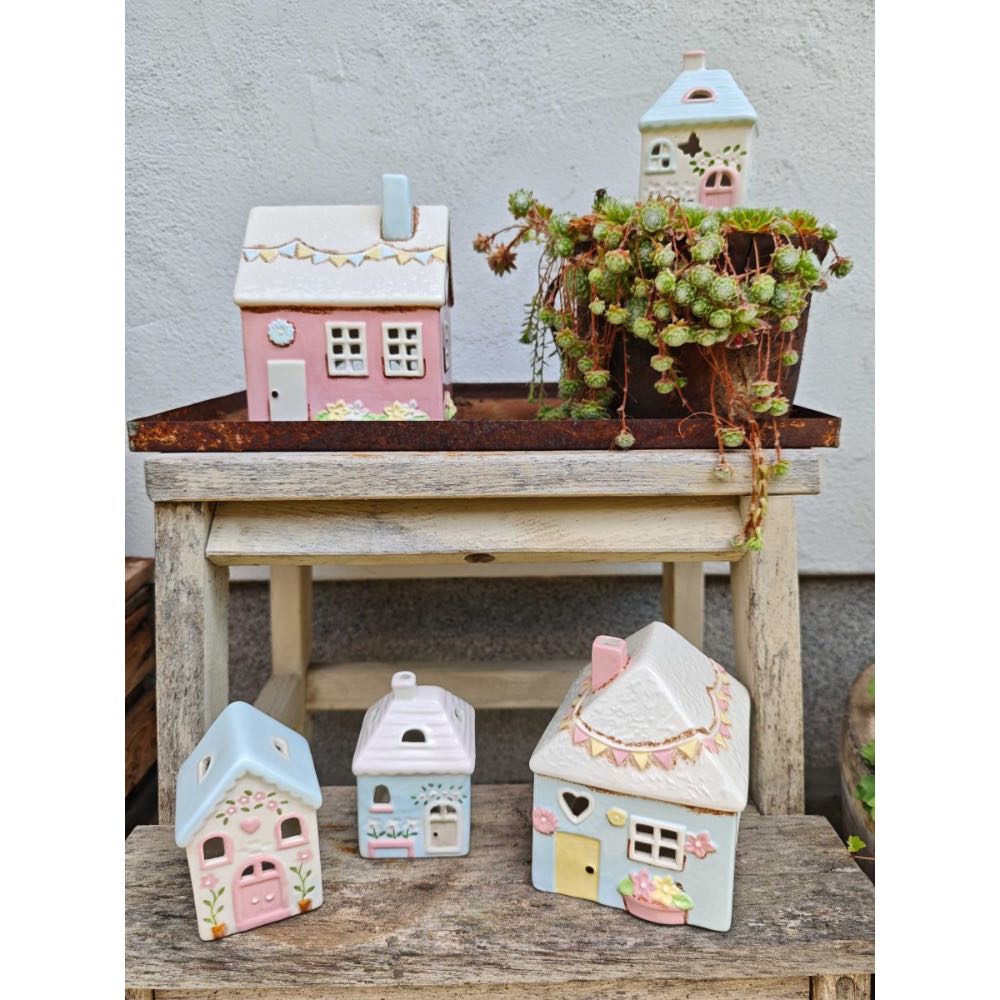 Vier Teelichthalter aus Keramik von Isabelle Rose im charmanten Landhausstil, die auf und vor einem Holzhocker angeordnet sind, stehen neben einer Topfpflanze mit grünen Blättern.