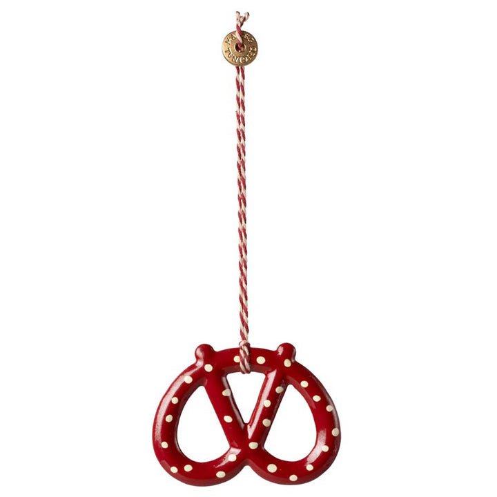 Der Maileg-Anhänger Brezel Metall besteht aus einem brezelförmigen Ornament mit einem rot-weißen Tupfenmuster, das an einer dazu passenden rot-weißen Schnur hängt und an deren Spitze sich ein kleines goldenes Etikett befindet.
