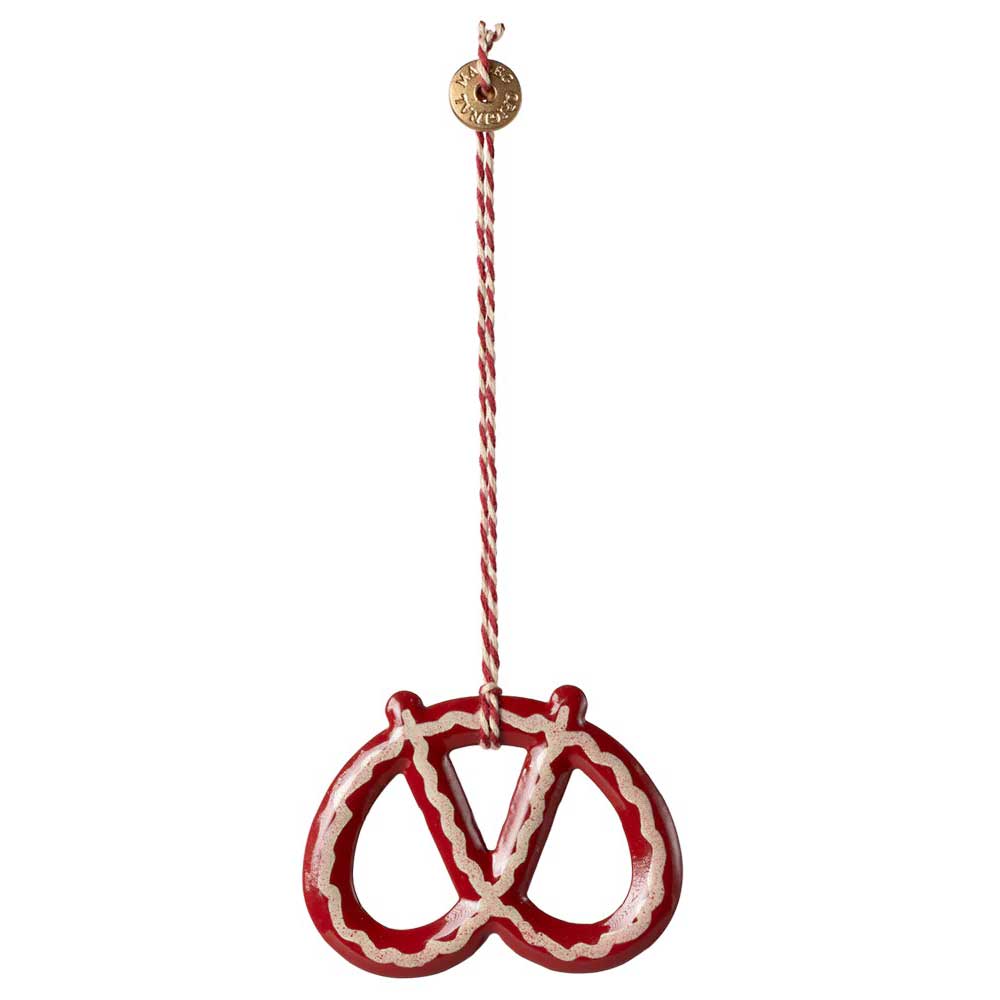 Der Maileg - Anhänger Brezel Metall ist ein brezelförmiges Ornament in Rot und Weiß, das an einer dekorativen Schnur hängt und an dem ein kleines rundes Etikett befestigt ist.
