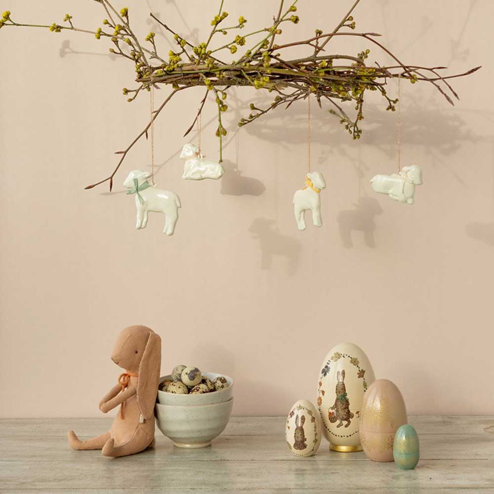 Eine pastellfarbene Osterkomposition mit hängenden Maileg - Anhänger Lamm Metall-Dekorationen, dekorativen Eiern und einem Plüschhasen.