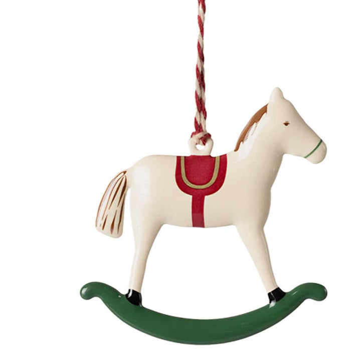 Der Maileg-Anhänger Metall Schaukelpferd ist ein bezauberndes Ornament im Design eines hölzernen Schaukelpferds mit weißem Körper, rotem Sattel, grünem Schaukelfuß und ist mit einer rot-weißen Schnur geschmückt.