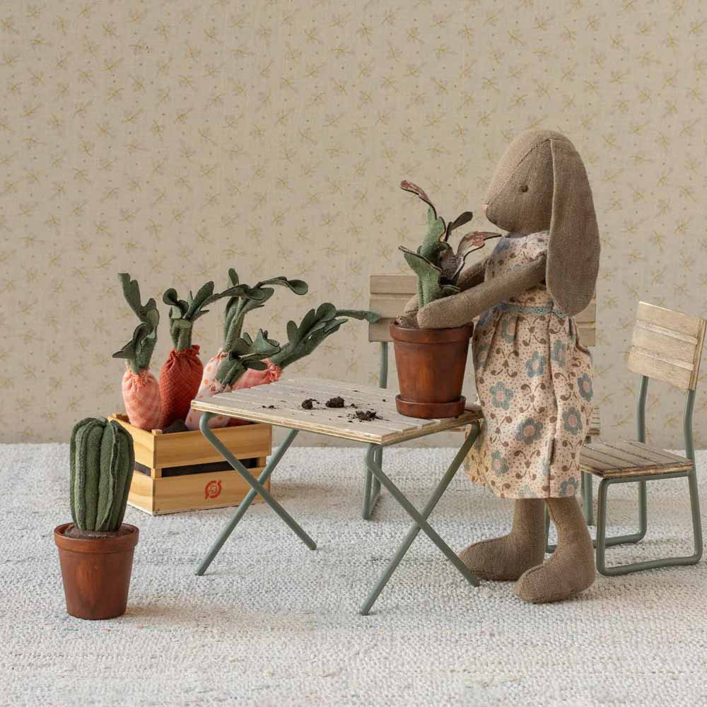 Der Maileg - Blumentopf mit Kaktus Miniatur zeigt ein ausgestopftes Kaninchen im Blumenkleid an einem kleinen Tisch, umgeben von Stoffgemüse und Holzstühlen in einer detaillierten Miniatur-Zimmerszene.